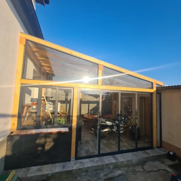 Detailný pohľad na zasklenie drevenej pergoly pri dome v Holíči, svetlohnedá farba RAL 8003.