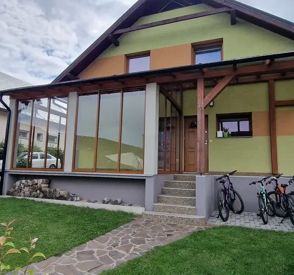 Celkový pohľad na zasklený prístrešok na terase v Lokca, posuvný hliníkový systém vo farbe RAL 8003 bledá hnedá.