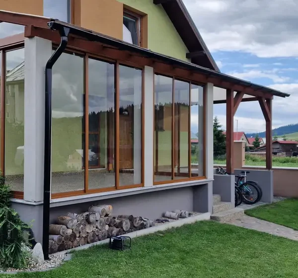 Pohľad z exteriéru na zasklený prístrešok na terase v Lokca, posuvný hliníkový systém vo farbe RAL 8003 bledá hnedá.