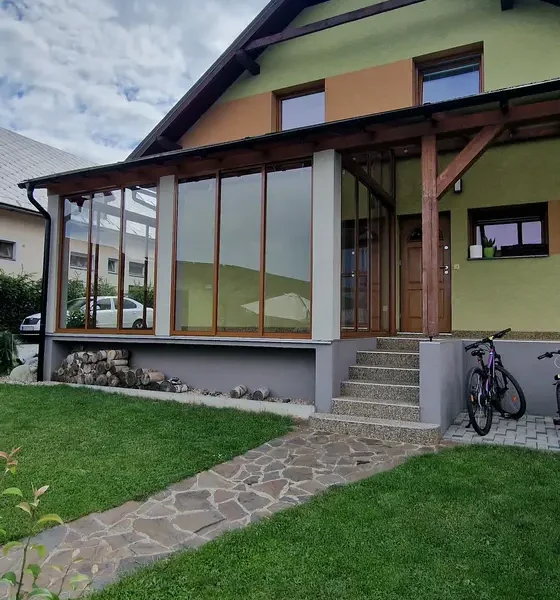 Celkový pohľad na zasklený prístrešok na terase v Lokca, posuvný hliníkový systém vo farbe RAL 8003 bledá hnedá z diaľky.