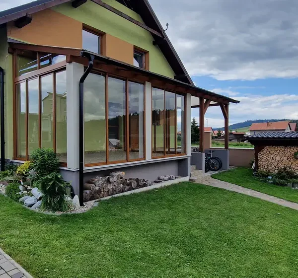 Bočný pohľad na zasklený prístrešok na terase v Lokca, posuvný hliníkový systém vo farbe RAL 8003 bledá hnedá.
