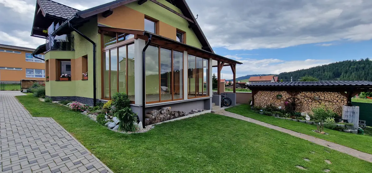 Bočný pohľad na zasklený prístrešok na terase v Lokca, posuvný hliníkový systém vo farbe RAL 8003 bledá hnedá.