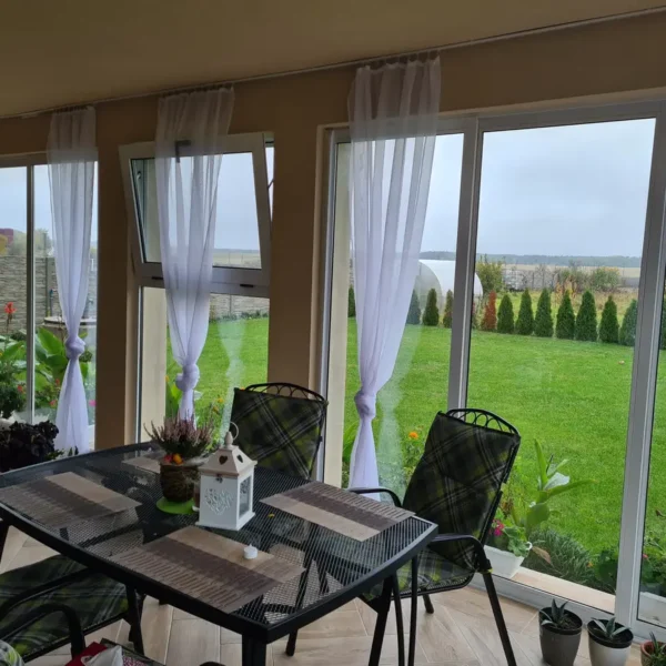Interiér zasklenej terasy s bielym hliníkovým systémom v Čároch, pohľad na záhradu.
