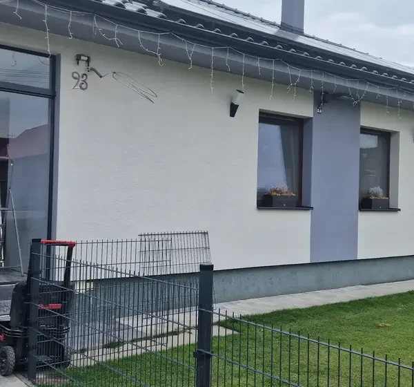 Zasklenie vchodu do rodinného domu v Ležiachove počas inštalácie, pracovník zametá pred vstupom.