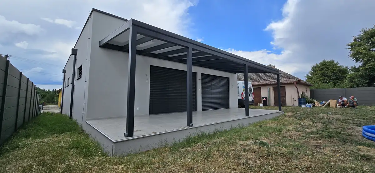 Bočný pohľad na hliníkovú pergolu s rozmermi 10 x 3,2 m v Šajdíkových Humenciach, ktorá poskytuje tienistý priestor pre vonkajšie aktivity.