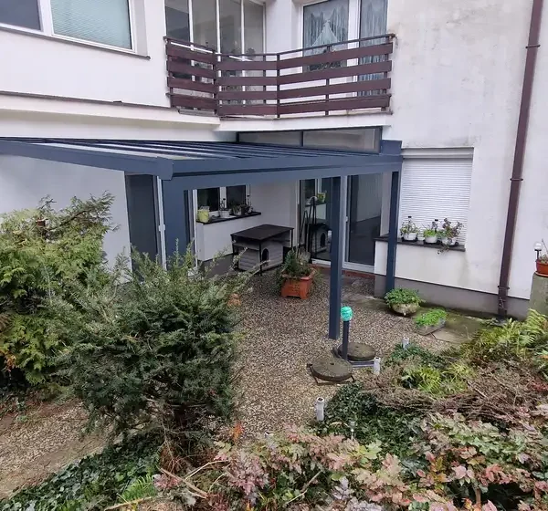 Pohľad z vnútra pod hliníkovou pergolou 7 x 3 m pri rodinnom dome v Bratislave, ukazujúci výhľad do záhrady.
