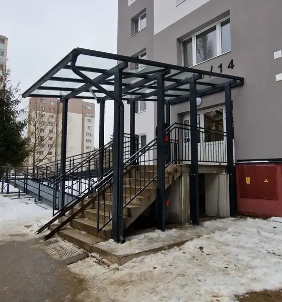 Detail oceľového prístrešku s bezpečnostným sklom pred vchodom do bytovky v Považskej Bystrici, zábradlie v antracitovej farbe RAL 7016.