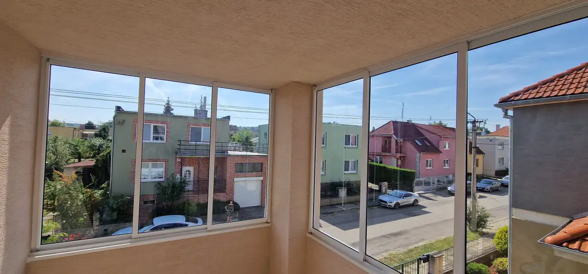 Zasklenie balkónu na rodinnom dome v Skalici, s čírymi sklenenými panelmi v bielom hliníkovom ráme (RAL 9003), poskytuje nerušený výhľad na okolitú štvrť.