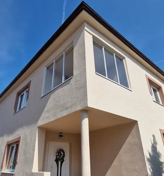Exteriérový pohľad na rodinný dom v Skalici s novo nainštalovaným zasklením balkónu, ktorý disponuje bielym hliníkovým systémom (RAL 9003) dokonale zapadajúcim do architektúry domu.