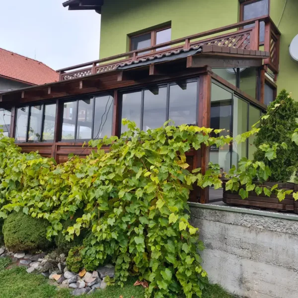 Predný pohľad na zasklenie drevenej terasy pod balkónom v Beňuši, kde je použitý izolačný dvojsklenný systém a dvere v antracitovej farbe.