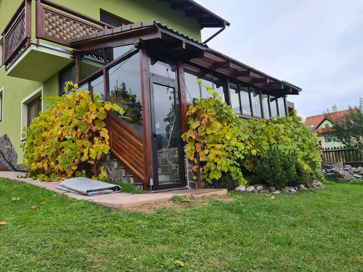 Zadný pohľad na zasklenú drevenú terasu pod balkónom v Beňuši, s rámovým posuvným systémom RAL 7016 v antracitovej farbe.