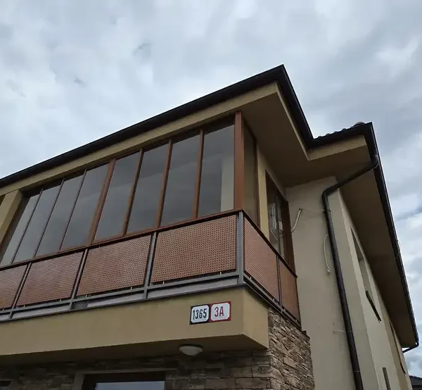 Exteriérový pohľad na zasklený balkón v obci Veľký Biel s bledohnedým hliníkovým systémom, odtieň RAL 8003.