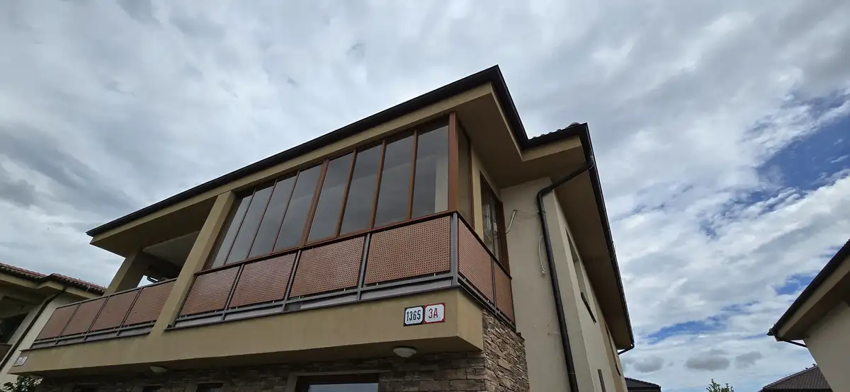 Exteriérový pohľad na zasklený balkón v obci Veľký Biel s bledohnedým hliníkovým systémom, odtieň RAL 8003.